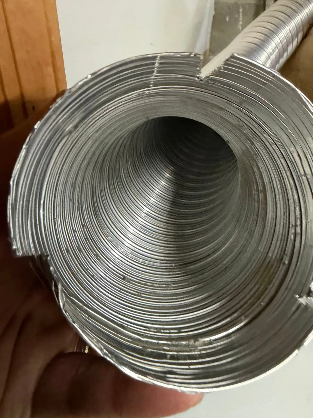 A coil of flexible aluminum duct held open in one hand.